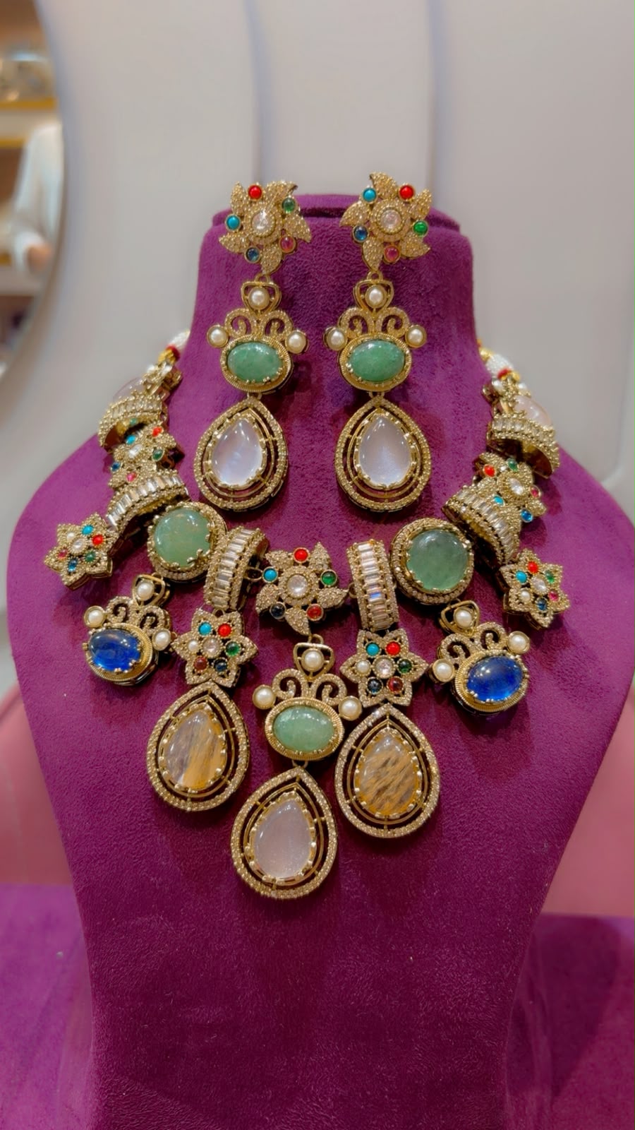 Sabyasachi-style multi-stone fusion necklace set displayed on purple bust showing jade green, blue, and quartz gemstone drops.